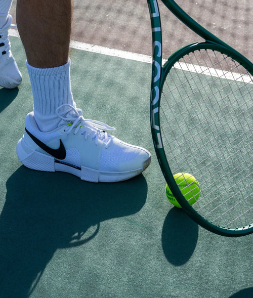 man holding tennis racket with restring sync strings next to tennis ball