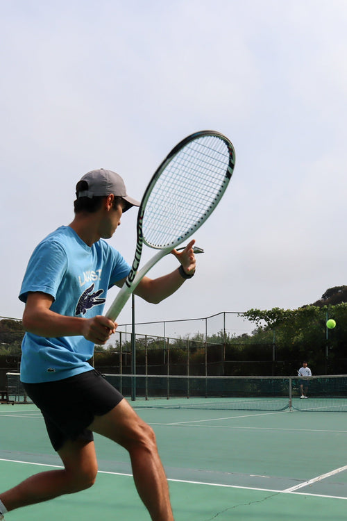 man holding a tennis racket with copoly strings playing tennis getting ready to hit a tennis ball