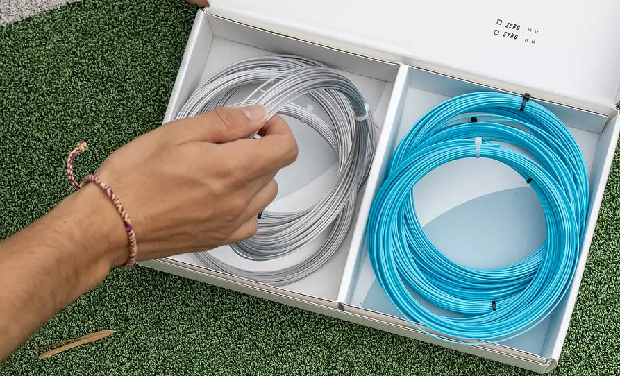 man holding Sync tennis string in front a tennis string box
