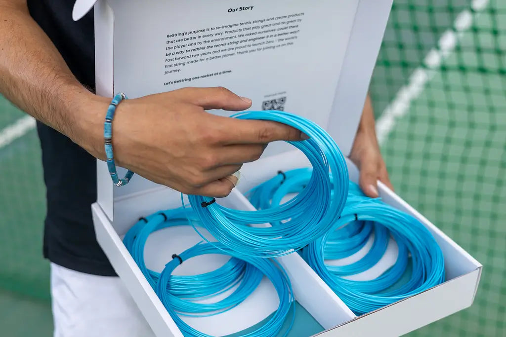 man holding box of Zero tennis strings with Zero bracelet on
