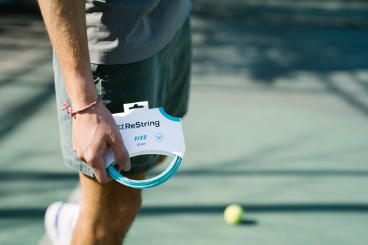 man holding restring vivo tennis string playing style on tennis court with tennis ball in the background