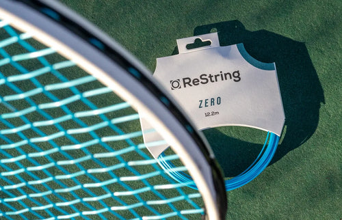 tennis racket next to restring zero string on a hard tennis court