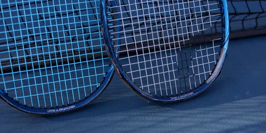 two tennis rackets on a blue court resting against the net